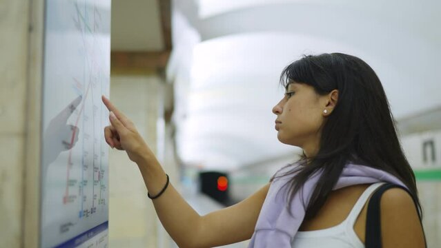 A young woman in the subway looks at the subway map on the wall, runs her finger along it. Slow motion 120fps footage
