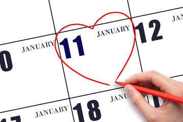 A woman's hand drawing a red heart shape on the calendar date of 11 January. Heart as a symbol of love.