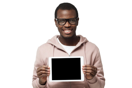 Horizontal shot of young African man pictured with trendy eyeglasses on presenting blank tablet screen to viewers with smile