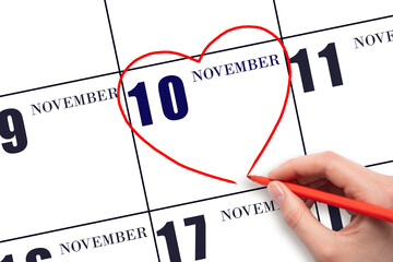A woman's hand drawing a red heart shape on the calendar date of 10 November. Heart as a symbol of love.
