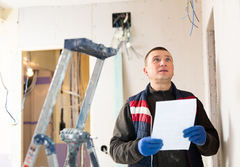 Professional builder standing at indoors building site, reading document