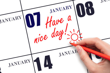 The hand writing the text Have a nice day and drawing the sun on the calendar date January 7