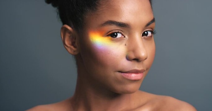 Rainbow, Prism And Light On Face Of Black Woman For Glow, Beauty Or LGBT Pride Against A Grey Background In Studio. Holographic, Flare And Reflection On Young Female For Art, Creative Or Skincare