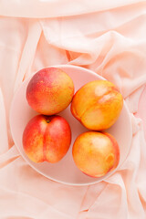 Fresh nectarines in a plate on pink textile background, high angle view.