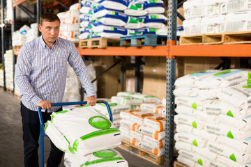 Satisfied smiling Man choosing compost soil in plastic bags in hypermarket .