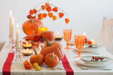 autumn table setting with burning candles and pumpkins