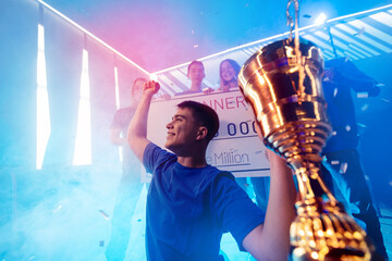 Winner team gamer, happy young man holding cup trophy prize of victors video games tournament esport. Soft focus motion blur, neon color © Parilov