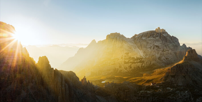 View from above, stunning aerial view of a mountain range during a beautiful sunrise with a mountain hut in the distance. Tre Cime di Lavaredo, Dolomites, Italy