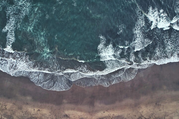 Big waves crushing on a sandy beach - blue green ocean captured with a drone - Canggu Bali