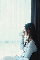 woman doing sitting at window after wake up with coffee mug