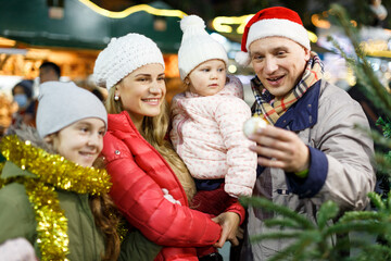 Portrait of smiling man and his happy wife and daughters buying tree at Christmas market