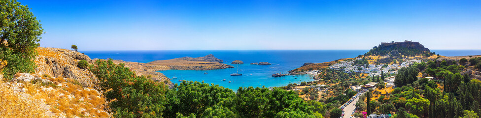 Naklejka na ściany i meble Panoramic view of colorful harbor in Lindos village and Acropolis, Rhodes. Aerial view of beautiful landscape, ancient ruins, sea with sailboats and coastline of island of Rhodes in Aegean Sea