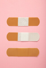 Beige adhesive bandages on pink background. Medical plasters. Vertical photo