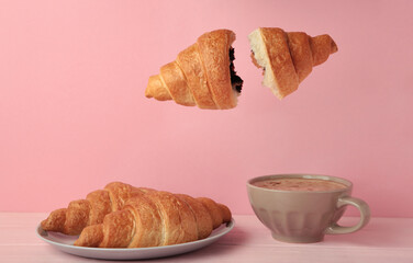 Flying croissant with coffee on pink background.