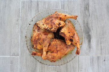 Four seasoned roasted whole chicken legs in a glass heat-resistant vessel, the grey wooden background