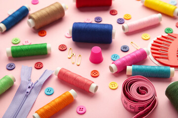 Sewing supplies on pink background: sewing thread, scissors, a large spool of thread, pieces of...