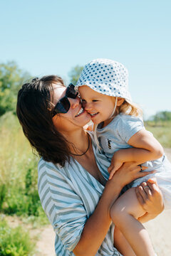 Loving mom with little daughter outdoors. Cheerful happy family, mother hugging, kissing the child