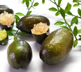 Edible fruits of Citrus australasica, the Australian finger lime or caviar lime. Whole limes on thorny branch and cut with vesicles partially extracted. Objects on white