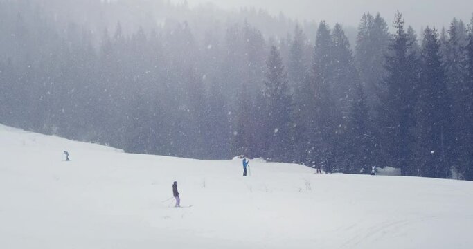 Snowy mountains landscape of ski resort. Beautiful snow falling, people moving down, slide of snow-covered slope. Spruce fir forest silhouettes. Winter holidays vacation recreation. Christmas weekend