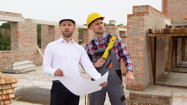 Two construction workers look at an architectural drawing in house construction