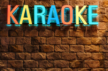 Colorful neon illuminated Karaoke sign on stone building wall background. Architectural decor of entertainment facilities. Singing karaoke concept.
