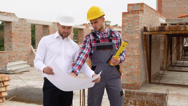 Two construction workers look at an architectural drawing in house construction