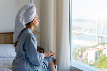 a young woman in a blue bathrobe and a white towel on her head lies on the bed of a hotel room and...