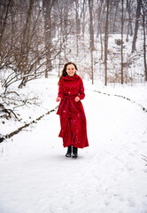 Fototapeta na wymiar beautiful smiling happy woman in red long dress having fun with snow in winter forest