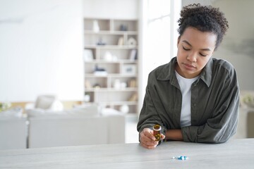 Pensive young mixed race girl holding jar with medicines doubting whether to take medical pills