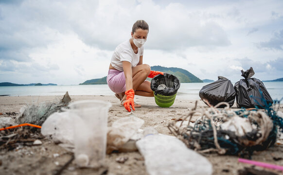 A female ecologist volunteer cleans the beach on the seashore from plastic and other waste