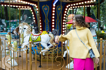 Fototapeta na wymiar Portrait of a young happy woman on the background of a carousel in an amusement park