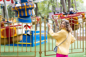 Woman in an amusement park look on a carousel and smiles with happiness, the concept of weekends