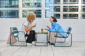 Happy young female models meet together at cozy cafeteria communicate with each other and discuss common startup have friendly meeting eat fresh salad and drink coffee have pleasant conversation