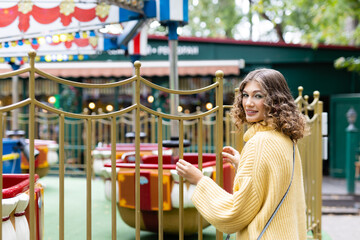Woman in an amusement park look on a carousel and smiles with happiness, the concept of weekends