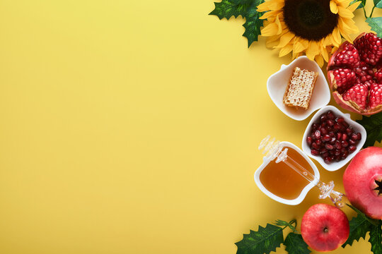 Rosh Hashanah. Ripe pomegranate, apple, honey and sunflower, yellow flowers on yellow background. composition with symbols jewish Rosh Hashanah holiday attributes. Top view with copy space.