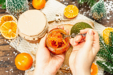 Woman's hands hold orange marmalade or orange jam in a glass jar. Sweet confiture with festive Christmas decor.
