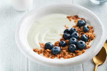 Yogurt. Greek Yogurt with granola and fresh blueberries in white bowl over old white wood background. Morning breakfast concept. Healthy food for breakfast, top view