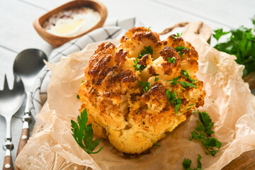 Baked cauliflower. Oven or whole baked cauliflower spices and herbs server on wooden rustic board on old white wooden background table. Delicious cauliflower. Eyal Shani dish. Perfect tasty snack.
