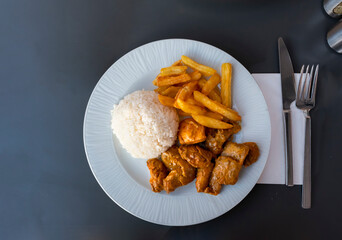 Chicken in curry sauce, rice, french fries in plate on table. Top view