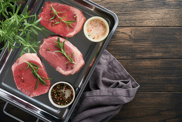 Steaks. Fresh Filet mignon Steaks with spices rosemary and pepper in kitchen tray on old wooden background. Top view.