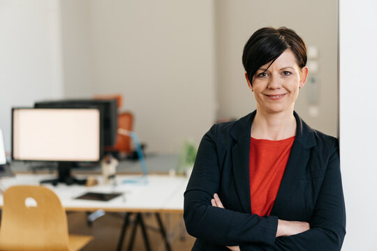 Businesswoman standing in office with arms crossed and smiling at camera