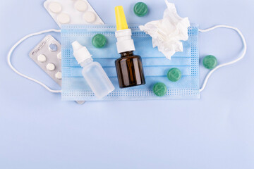 The concept of runny nose, flu, SARS, colds and coronavirus (COVID-19). Bubbles with nasal drops, protective mask, pills, handkerchiefs on a blue background. Space for text.