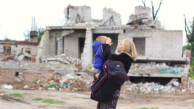 War. Kid and mother with a bag with things near a broken, shelled house in the background