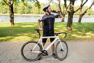 A male cyclist in a helmet drinks water from a bottle.
