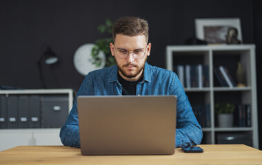 Portrait of young focused man coding on laptop, IT programmer working on creating innovative software, app, program.