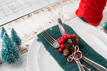 Christmas table setting with white dishware, silverware and red and green decorations on white...