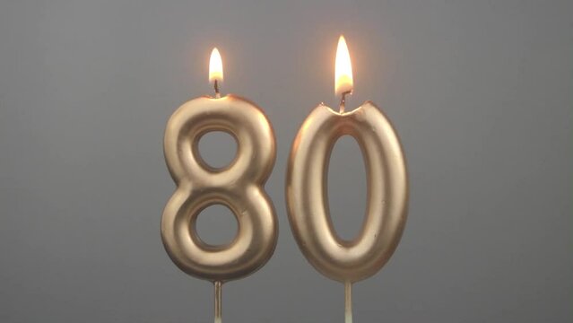 Burning gold birthday candles on gray background, number 80