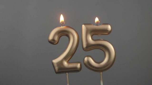 Burning gold birthday candles on gray background, number 25
