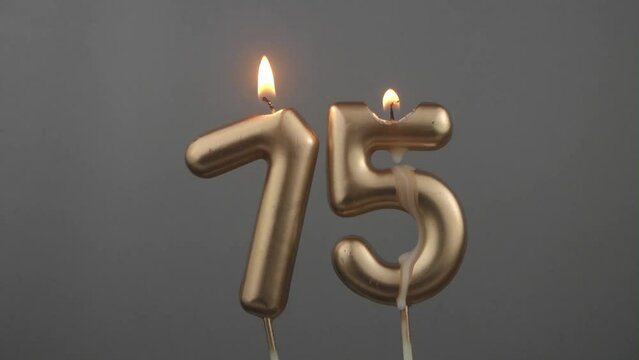 Burning gold birthday candles on gray background, number 75