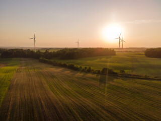 Obraz premium Green energy concept. Aerial cinematic drone panoramic shot of windmills and electricity wind turbines farm during summer sunset. Panoramic European nature view. Image contain noise and blur